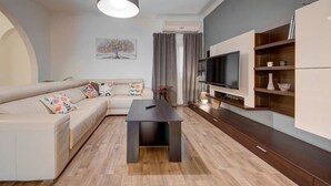 A modern living room with a sectional sofa, a dark coffee table, a flat-screen TV, and built-in shelving. - Charming home Apt with private balcony in B`Bugia (Birżebbuġa)