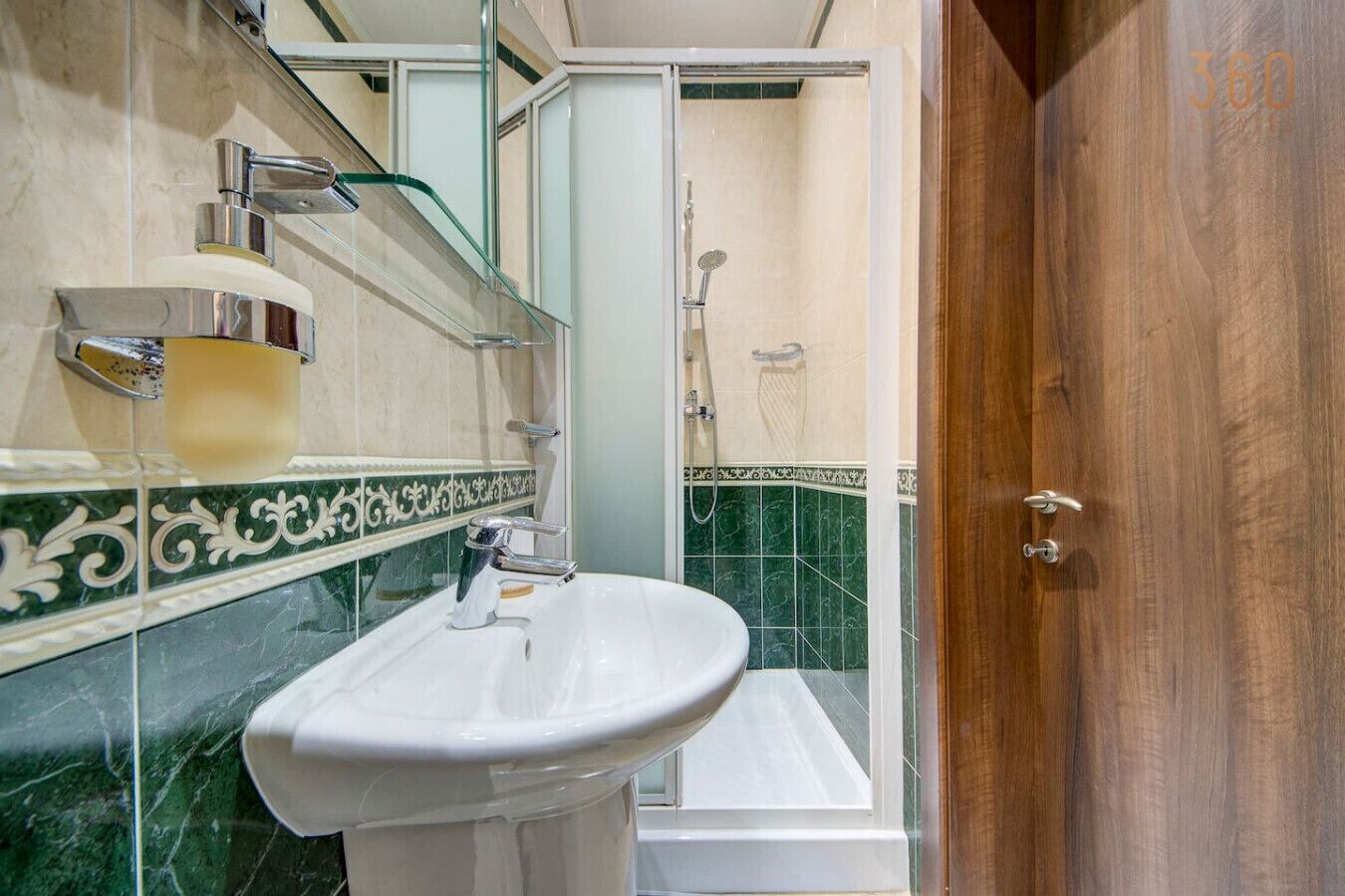 Un baño con un lavabo blanco, un cerramiento de ducha de vidrio y una puerta de madera.