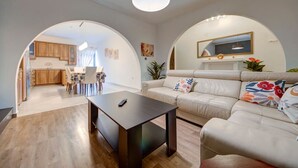 A modern living room with a sofa, a coffee table, and a TV. There is a kitchen visible through an archway. - Charming home Apt with private balcony in B`Bugia (Birżebbuġa)