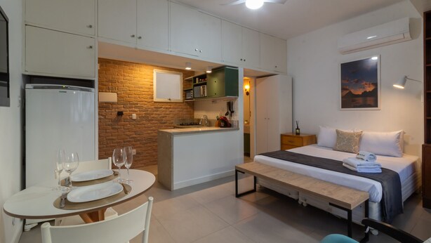 Una habitación de hotel pequeña con kitchenette, comedor y cama.