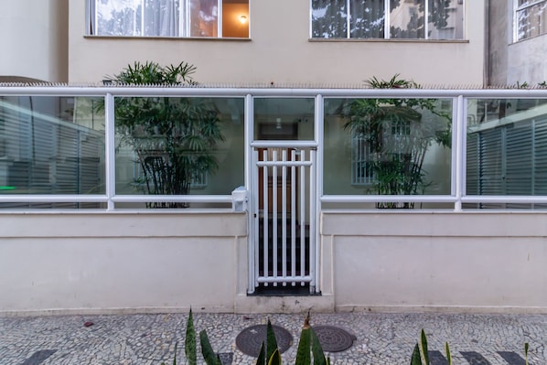 A building facade with a gated entrance, large windows, and potted plants.