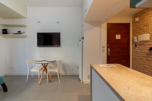 A modern kitchen with a built-in TV, a dining area with white chairs, and a stone wall. - 3 Minutes From Ipanema Beach Jn202 (Rio de Janeiro)