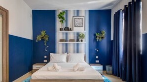 Un dormitorio con cama, ropa de cama blanca, pared a rayas azules y blancas y una ventana con cortinas.