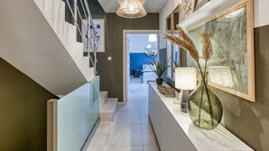 Un pasillo moderno con barandilla de vidrio, una escalera y vista a una habitación con pared azul.
