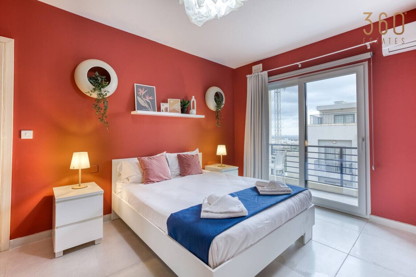 Un dormitorio moderno con una cama grande, mesitas de noche blancas y vistas de la ciudad desde un balcón.