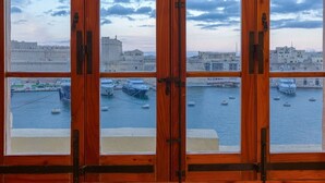 A view through a wooden-framed window of a harbor with boats, a large building, and a cityscape. - Maltese Maisonette in Historic Isla with Sea Views (L-Isla)