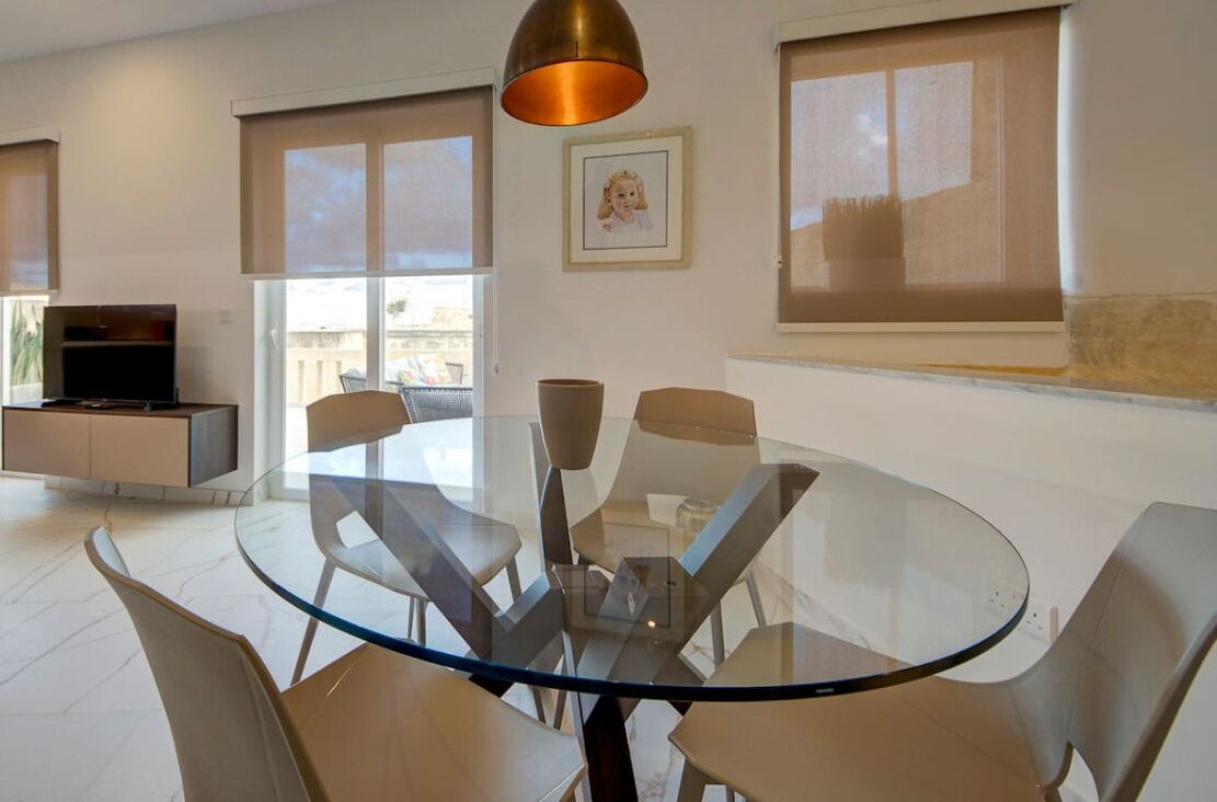 A modern dining area with a glass table and chairs, a television, and a view of the outdoors.