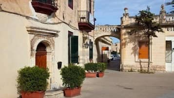 A street with historic buildings, a stone archway, and potted plants.
