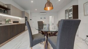 A modern kitchen with a built-in island, grey upholstered chairs, and a glass dining table. - Stylish 1BR Apt with sofabed & backyard, Attard (Attard)