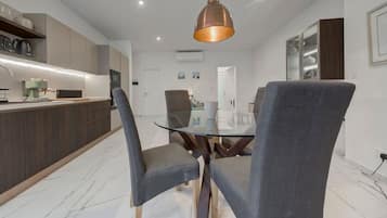 A modern kitchen with a built-in island, grey upholstered chairs, and a glass dining table.