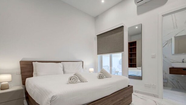 A modern bedroom with a large bed, bedside tables, a mirror, and an air conditioning unit. - Stylish 1BR Apt with sofabed & backyard, Attard (Attard)