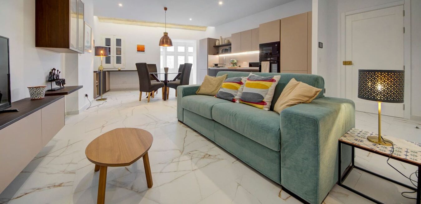 A modern living room with a green sofa, a wooden coffee table, and a dining area with chairs and a table.
