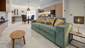 A modern living room with a green sofa, a wooden coffee table, and a dining area with chairs and a table. - Stylish 1BR Apt with sofabed & backyard, Attard (Attard)