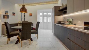 A modern kitchen with dark cabinetry, a round dining table, and a pendant light. - Stylish 1BR Apt with sofabed & backyard, Attard (Attard)