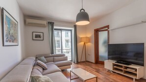 A modern living room with a sectional sofa, a flat-screen TV, a standing lamp, and a large window with curtains.