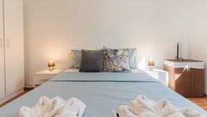 A bedroom with a bed, two bedside tables with lamps, a wooden cabinet, and a large window.