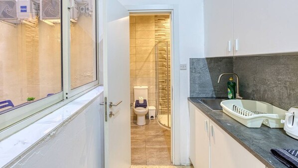 A modern kitchen with a sink, countertop, and a view of the bathroom through an open door. - Spacious 4BR Sliema Apt w/ Terrace & Top Location (Tas-Sliema)