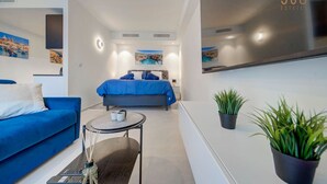 A modern hotel room with a bed, a blue sofa, a small table, and two potted plants. - Concierge Stay at Mercury Towers pjazza ! (San Ġiljan)