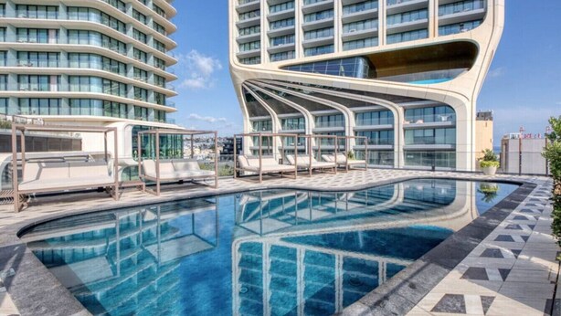 A modern hotel with a unique curved architecture, a rooftop pool area with lounge chairs, and a clear blue pool. - Concierge Stay at Mercury Towers pjazza ! (San Ġiljan)