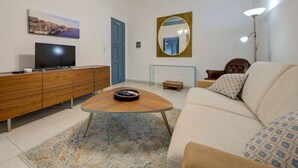 A living room with a sofa, coffee table, TV, wooden cabinet, and a mirror on the wall. - Cozy 3rd-Floor Valletta Apartment by the Seafront (Il-Belt Valletta)