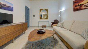 A modern living room with a wooden coffee table, a beige sofa, a TV on a wooden cabinet, and a painting on the wall. - Cozy 3rd-Floor Valletta Apartment by the Seafront (Il-Belt Valletta)