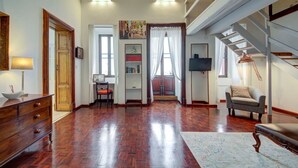 A spacious living room with hardwood flooring, a sofa, a chair, a wooden cabinet, a television, and a staircase. - Unique seafront Loft overlooking Valletta`s views (Il-Belt Valletta)
