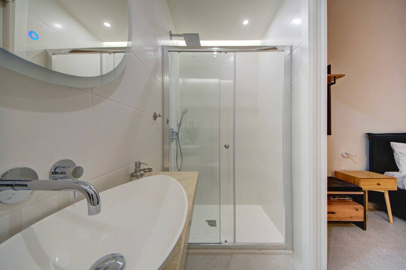Une salle de bain moderne avec une douche à parois de verre, un lavabo blanc et une table de chevet en bois.