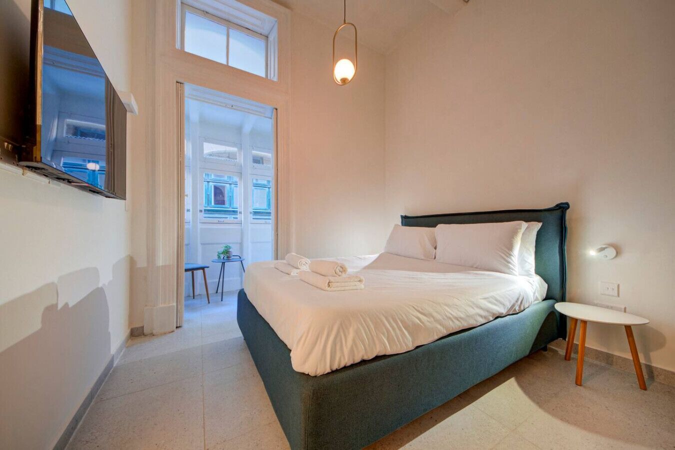 A bedroom with a bed, bedside table, and a view of the outside.