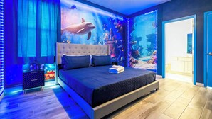 Quarto com cama grande, mesa de cabeceira e parede com aquário.