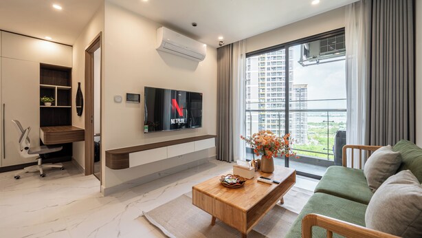Una sala de estar moderna con un televisor de pantalla plana, una mesa de centro de madera, un sofá verde y un ventanal con vistas a edificios.
