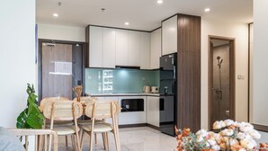 Cocina moderna con armarios blancos, horno empotrado y refrigerador. Hay un comedor con mesa y sillas, y un espacio de ducha con puerta de vidrio.