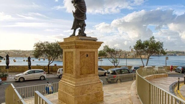 Eine Statue auf einem Sockel in einem öffentlichen Platz mit Blick auf das Wasser.