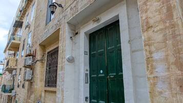 A building with a green door, a window, and an air conditioning unit on the wall.