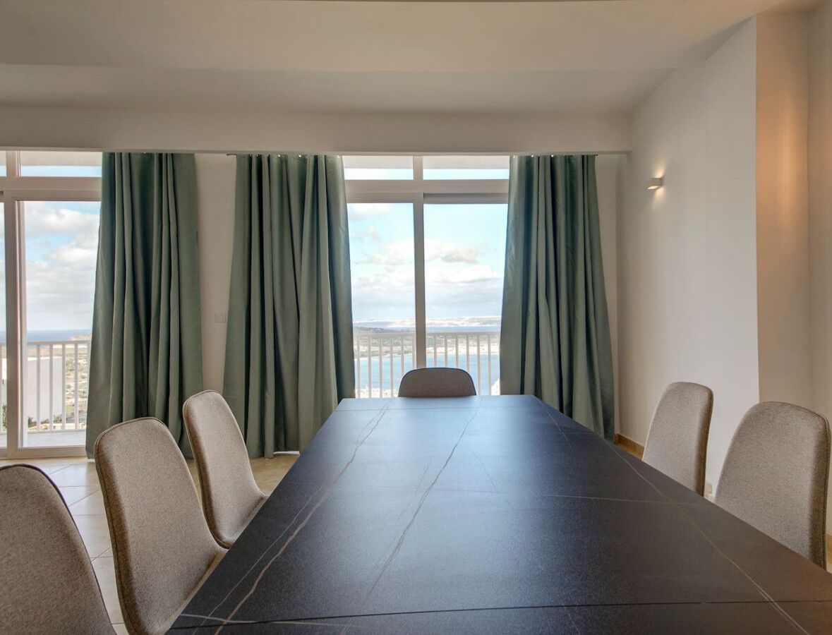 Una sala conferenze con un lungo tavolo e sei sedie, ampie finestre con tende e vista sul mare.
