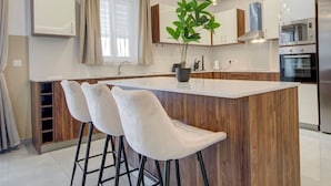 A modern kitchen with a central island, bar stools, a potted plant, and stainless steel appliances.