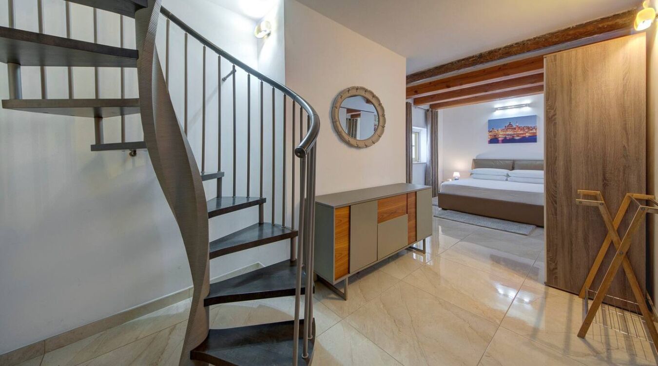 Habitación de hotel moderna con una escalera en espiral, una puerta de madera, una cama y un cuadro en la pared.