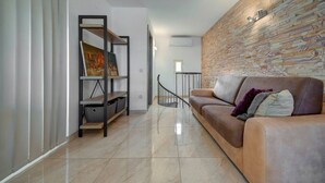 Een moderne woonkamer met een bruine leren bank, een houten boekenkast en een gestructureerde wand.