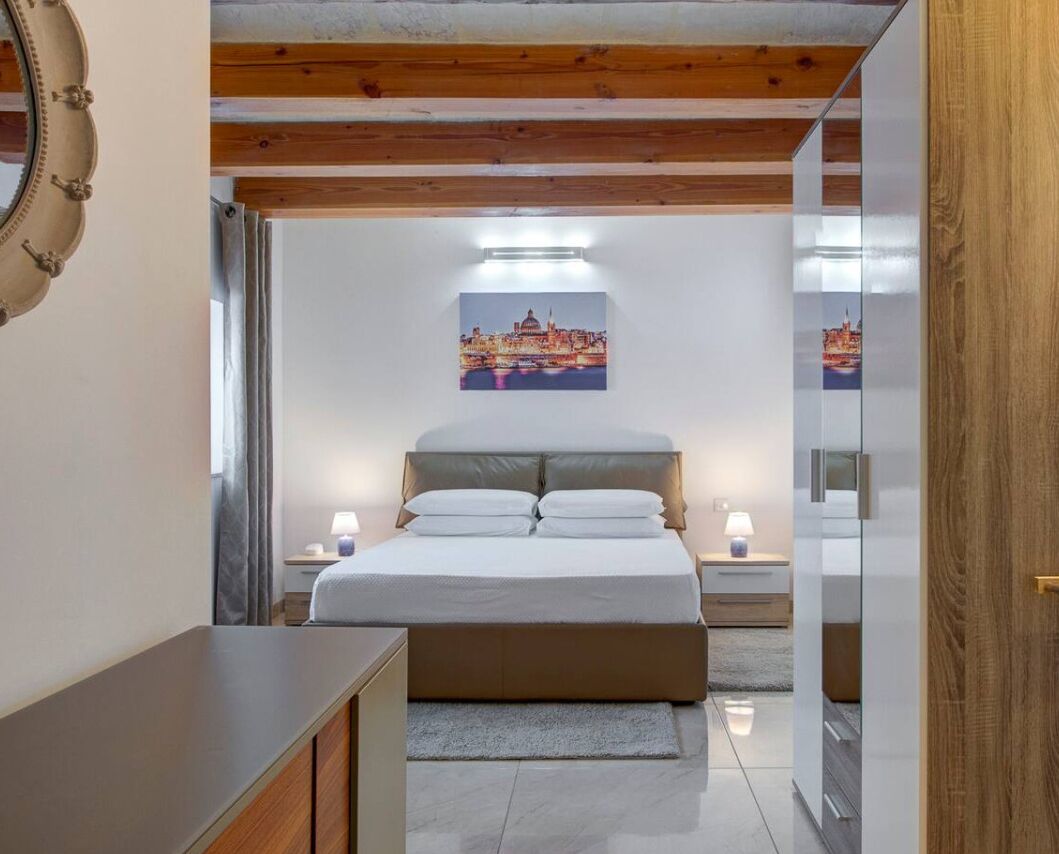 A bedroom with a bed, bedside tables, a nightstand, a wall-mounted picture, and a wooden ceiling.