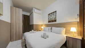Une chambre d’hôtel avec un grand lit, deux tables de chevet, une tête de lit, un climatiseur fixé au mur et un tableau au-dessus du lit.