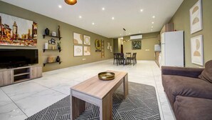 Un vaste espace de vie comprenant un téléviseur à écran plat, une table basse en bois et un canapé marron. On y trouve également plusieurs étagères murales et une table à manger avec des chaises.