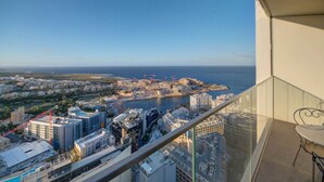 Un immeuble de grande hauteur offrant une vue sur le paysage urbain de la côte, notamment sur un port de plaisance et des grues de chantier.