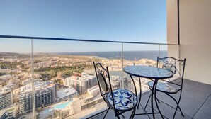 A balcony with a glass railing overlooking a cityscape and the sea.