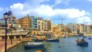 A waterfront with boats docked, buildings in the background, and a clear sky.