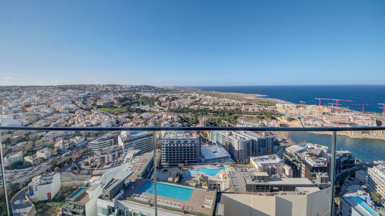 A high-rise hotel with a pool, overlooking a coastal cityscape and the sea.
