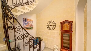A spiral staircase with ornate metal railings, a wall clock, a large wooden grandfather clock, and a statue.