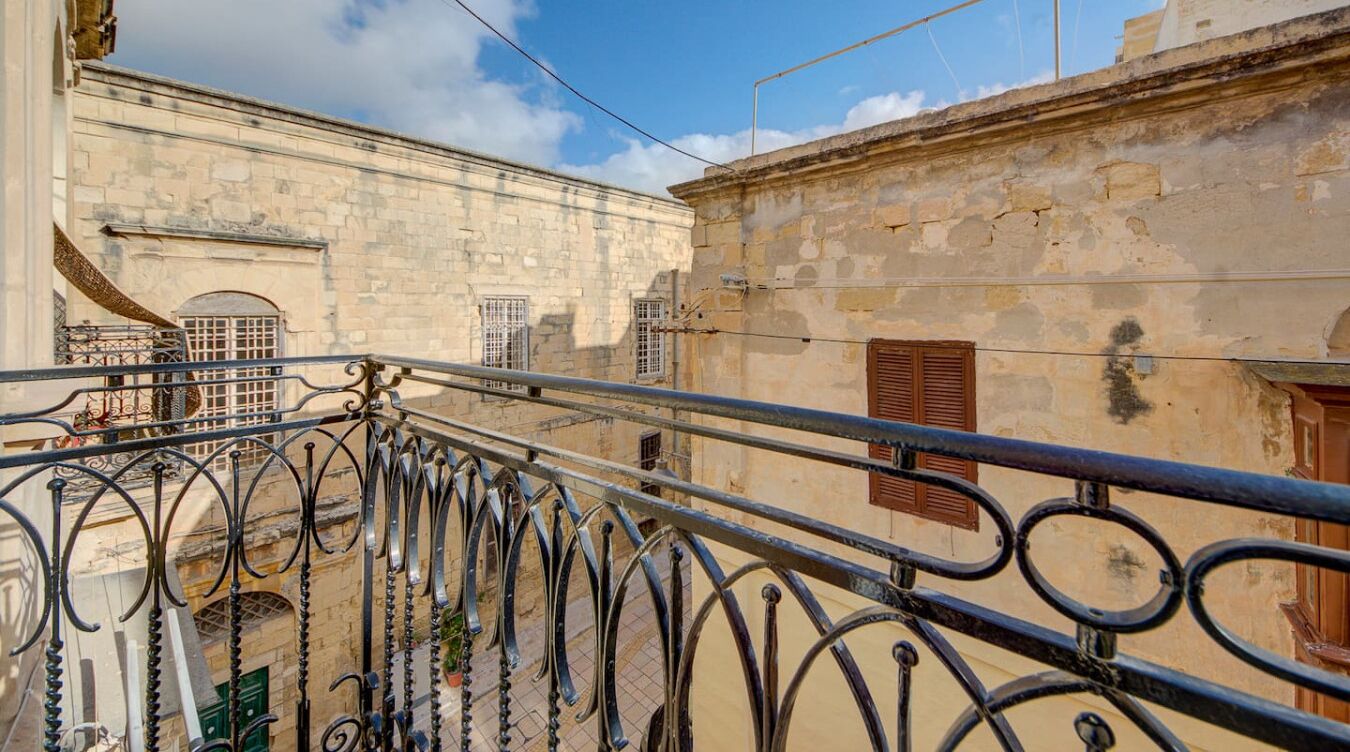 Un balcon doté de balustrades en fer forgé, donnant sur une cour intérieure bordée de bâtiments en pierre.