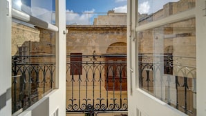 A view from a balcony with wrought iron railings, a stone wall, and a clear blue sky.