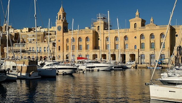 A marina with multiple boats docked, a prominent clock tower, and a large building with arched windows and balconies. - Cozy 1BR Apt in Birgu – Traditional Maltese Charm (Birgu)