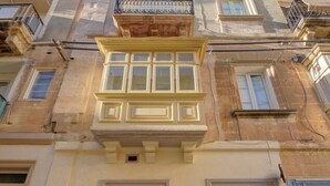 A building with a balcony, a window with shutters, and a door with a metal gate. - Cozy 1BR Apt in Birgu – Traditional Maltese Charm (Birgu)