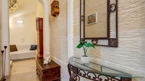 A hallway with a white sofa, a wooden cabinet, a glass table with a plant, and a mirror on the wall. - Cozy 1BR Apt in Birgu – Traditional Maltese Charm (Birgu)